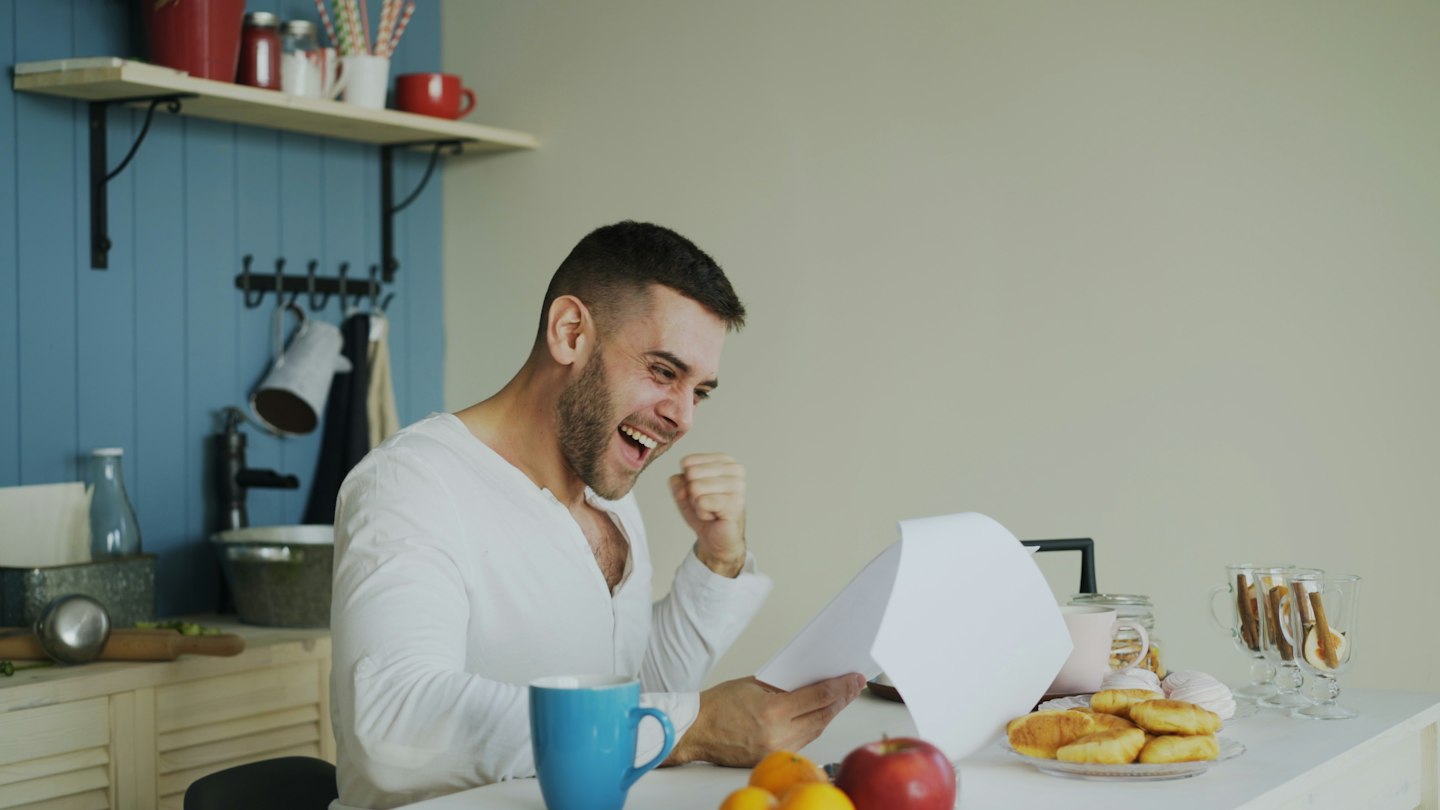 Man celebrating while reading a document at kitchen table