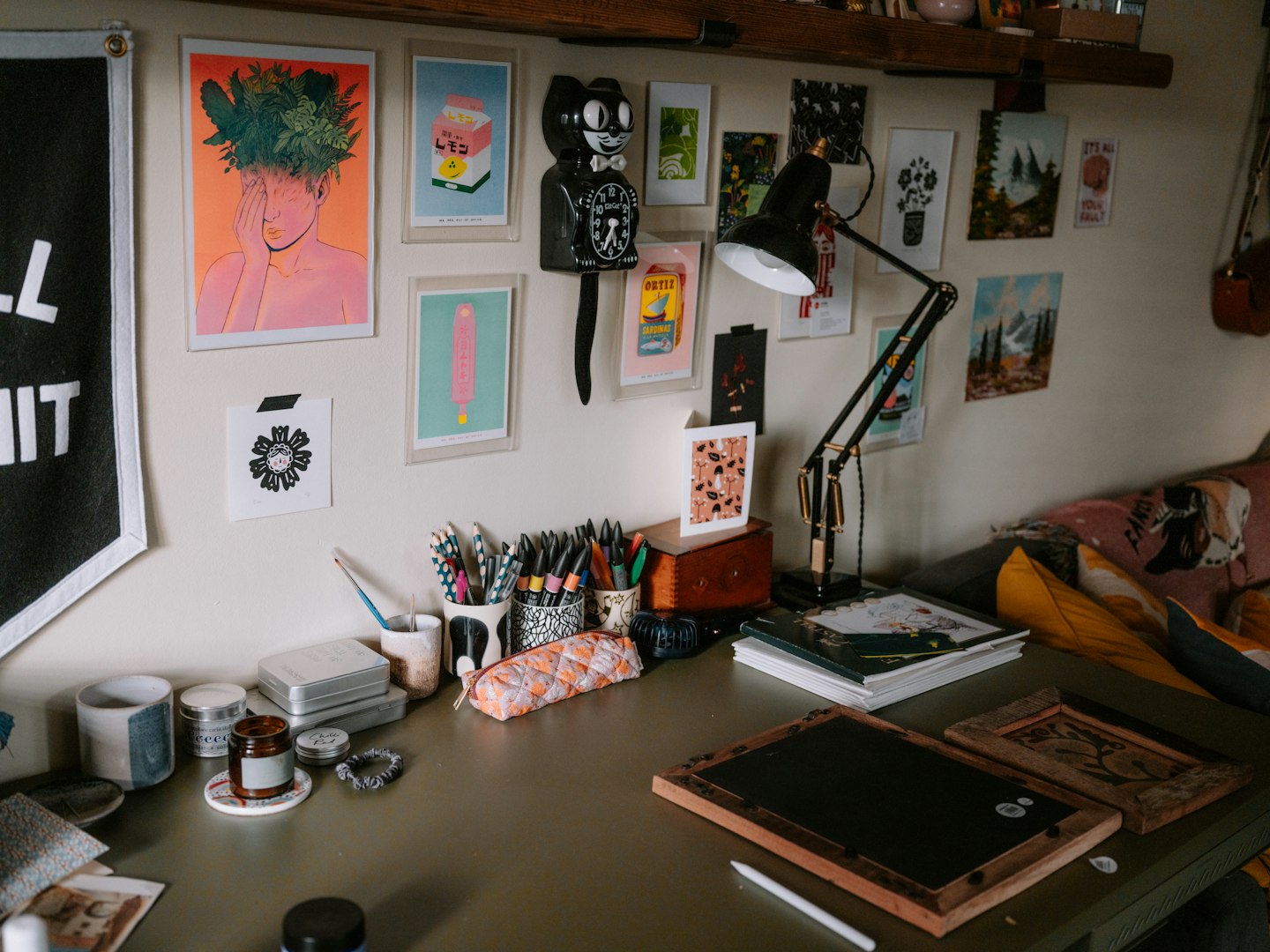 A desk with art supplies, a lamp, and a wall covered in small prints