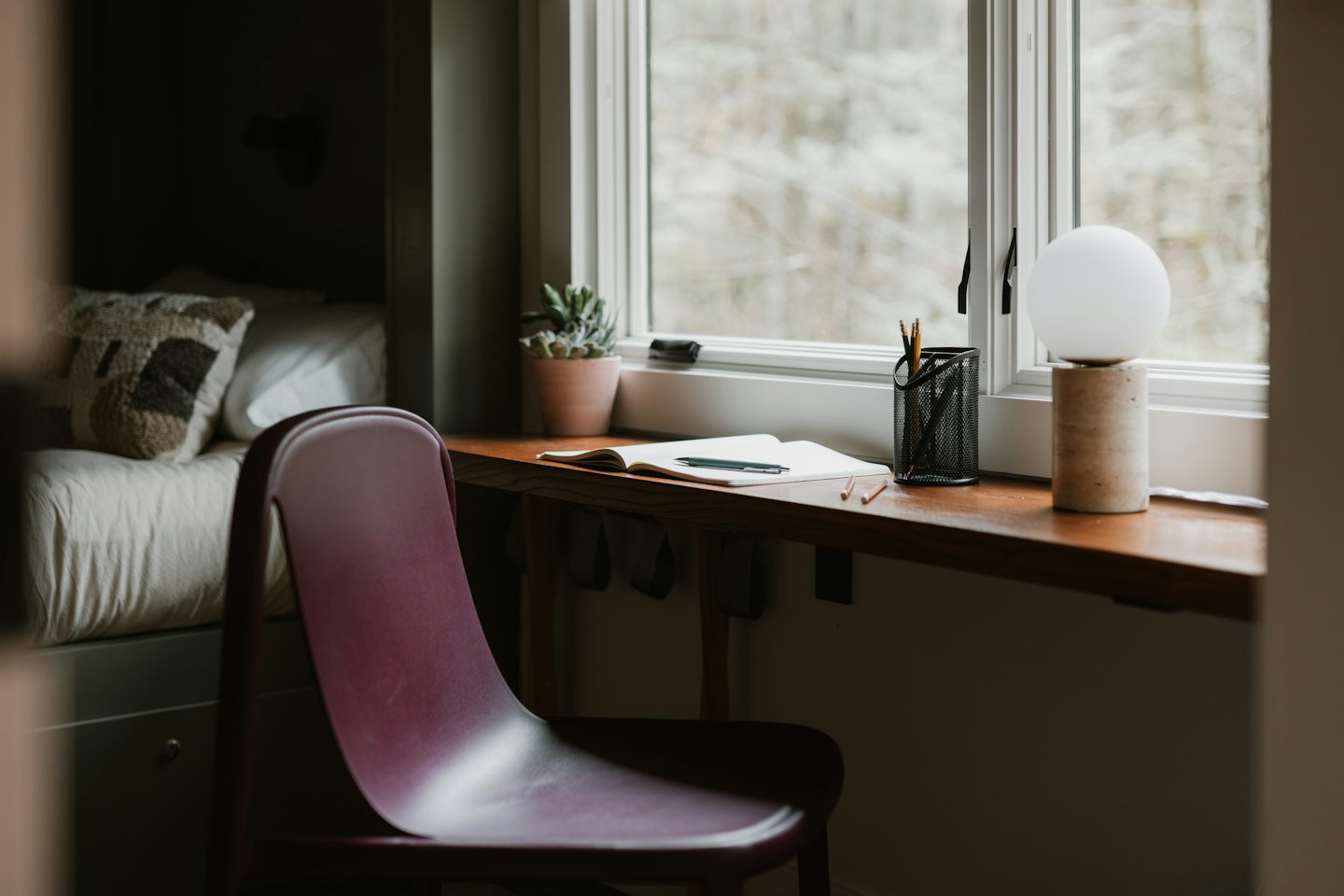 A chair and desk by a window with a lamp
